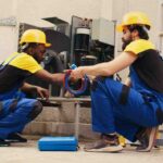 Two technicians in blue overalls working on an air conditioning unit at Mechanic Refrigeration and A.C.iti mrac