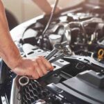 A man working on a car engine, focused on repairs as part of his mechanic training in motor vehicle maintenance.
